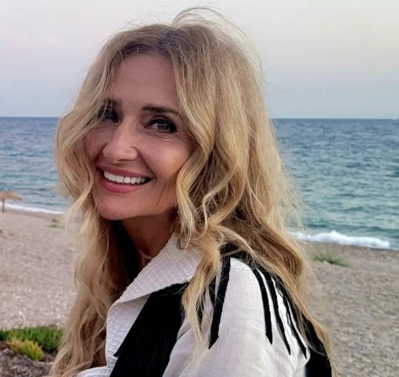 Vicky DeRosa beneath Greek flags by the Mediterranean